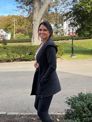 woman in a park turned to the side wearing an open activeear cardigan with a hood and black leggings