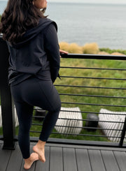 woman facing away weaing black leggings with pockets and a hooded black cardigan made from the same activewear fabric